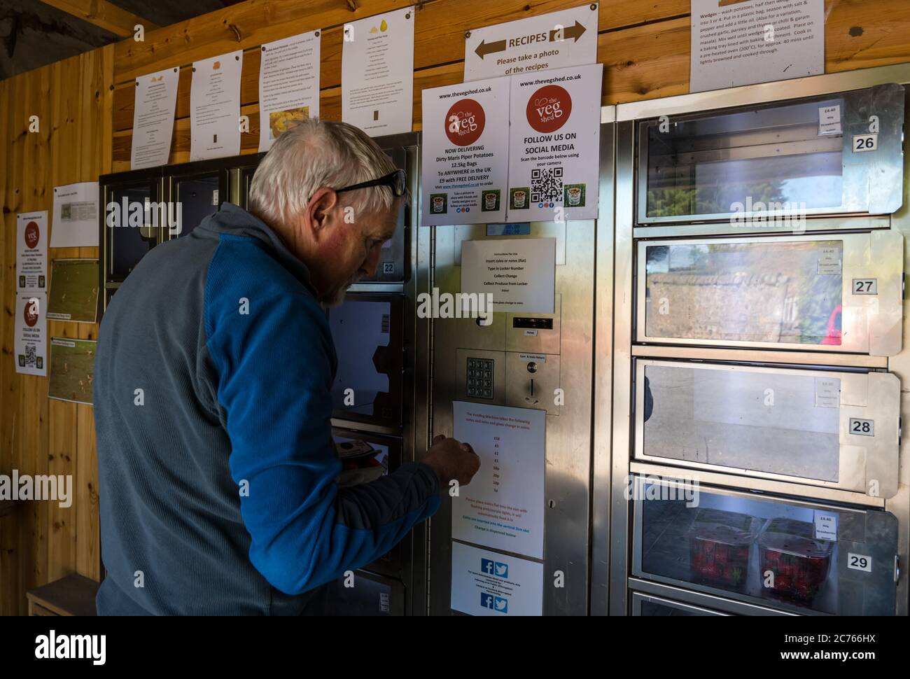 Homme senior insérant de l'argent dans un distributeur automatique pour les produits locaux au Veg Shed, à la ferme principale d'Athelstaneford, East Lothian, Écosse, Royaume-Uni Banque D'Images