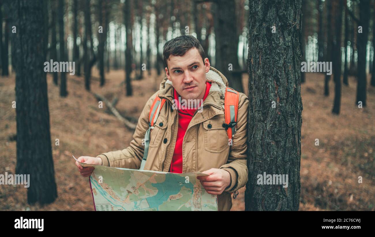 Un homme de voyage avec une carte dans les bois. Un portrait de l'homme beau avec un sac à dos, debout près d'un arbre par temps froid. Banque D'Images