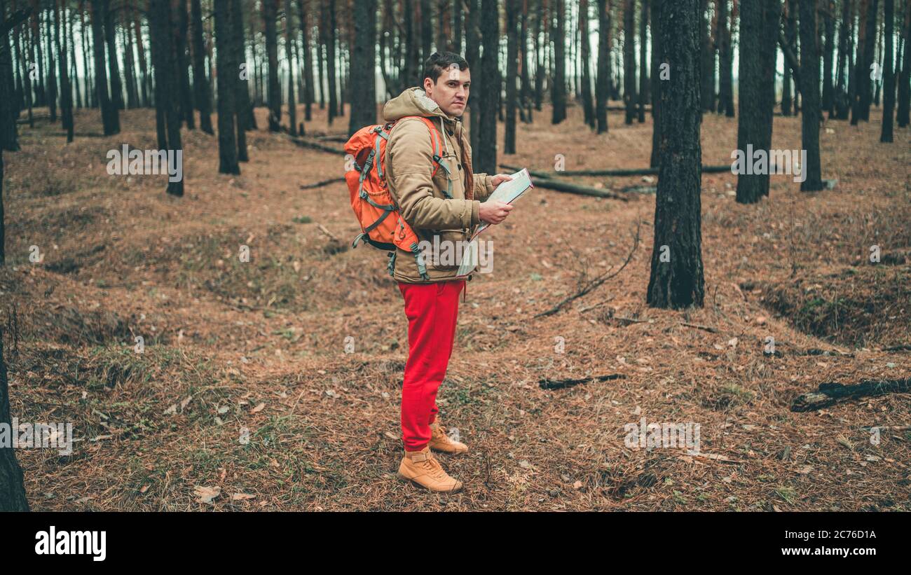 Un homme de voyage avec une carte dans les bois. Un portrait de l'homme beau avec un sac à dos, debout près d'un arbre par temps froid. Banque D'Images