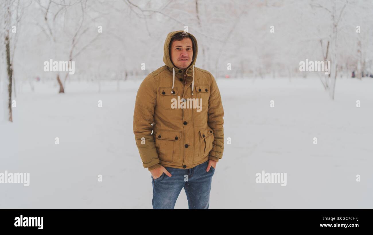 Portrait du jeune homme en veste et jeans en hiver. Beau homme se tient et s'accroupir dans le parc d'hiver. La neige douce enveloppe tout. Banque D'Images