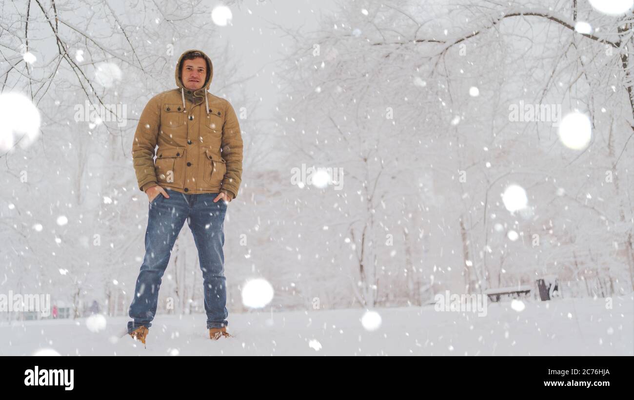 Portrait du jeune homme en veste et jeans en hiver. Beau homme se tient et s'accroupir dans le parc d'hiver. La neige douce enveloppe tout. Banque D'Images