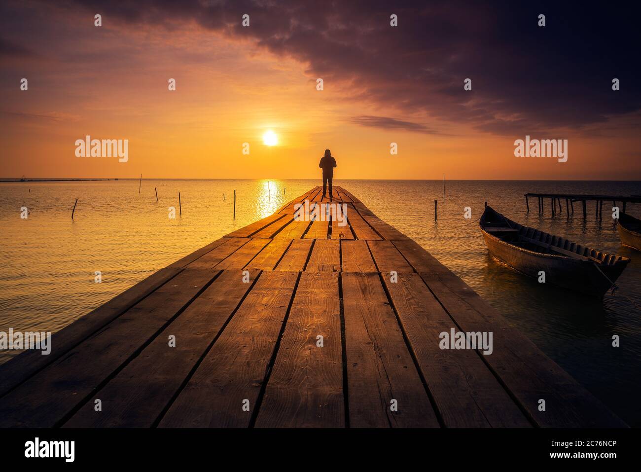 Personne seule debout sur un ponton méditant et appréciant le lever ou le  coucher du soleil sur un lac avec un bateau de pêche sur le lac Photo Stock  - Alamy