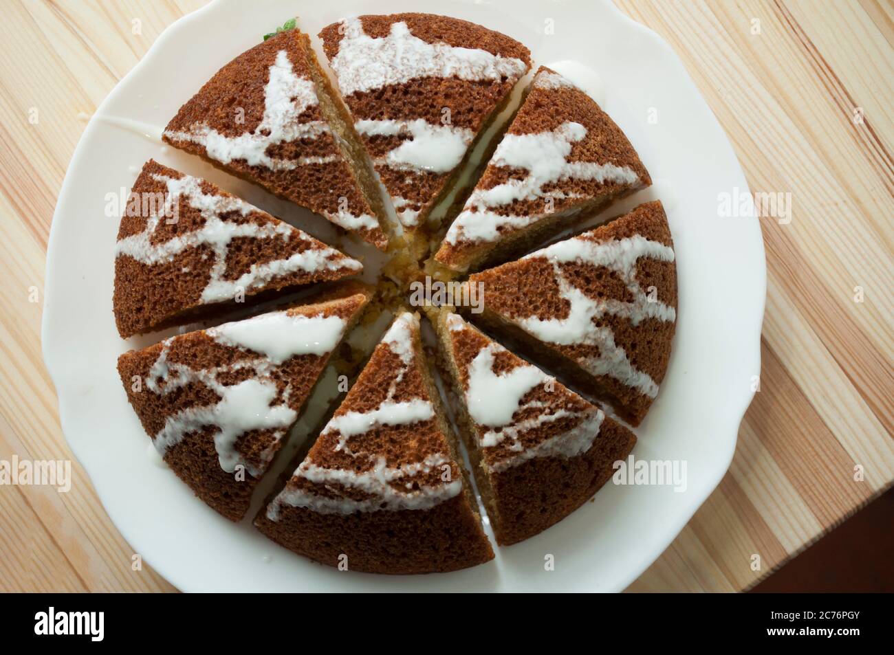 En tranches, le gâteau éponge est divisé en portion sur un fond en bois. Gâteau noir, arrosé de glaçage blanc. Minimaliste, macro photo, vue de dessus, Banque D'Images