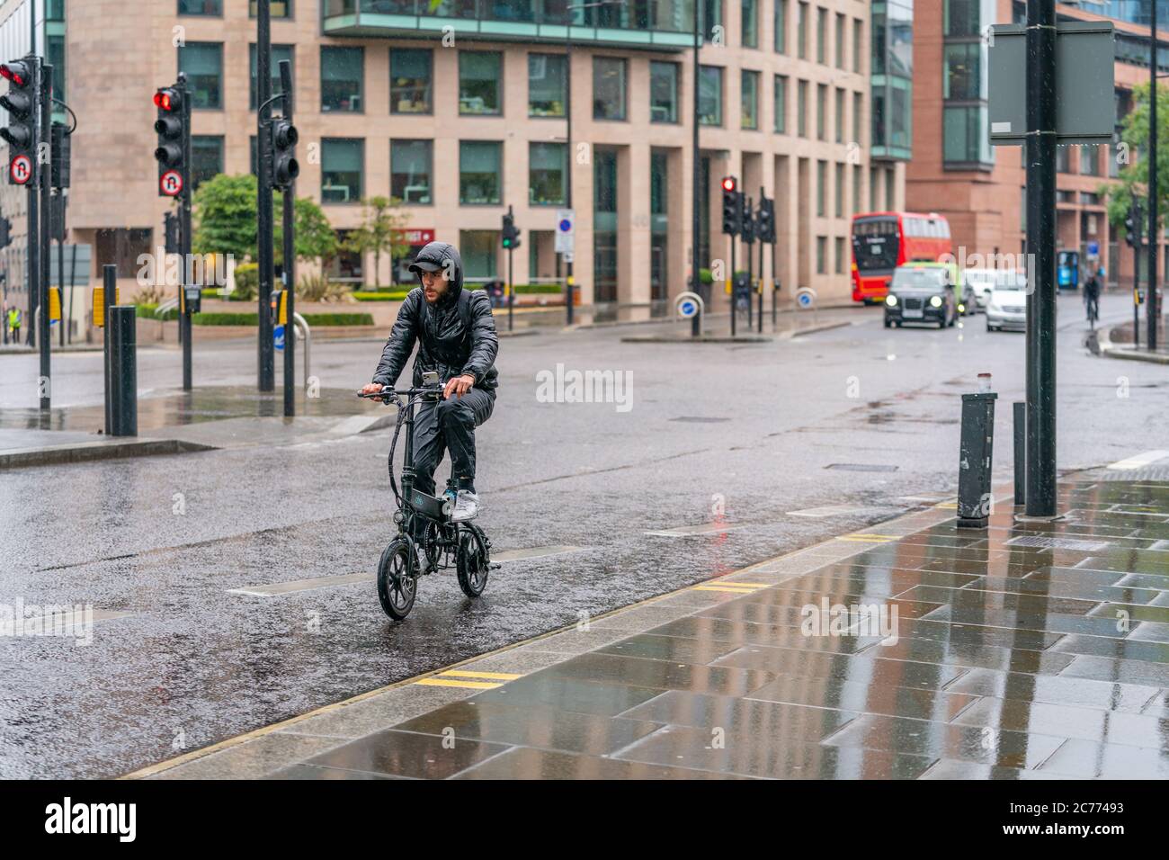 LONDRES, ANGLETERRE - 10 JUIN 2020 : un cycliste est pris dans la pluie par une journée de drizzly à bord d'un petit vélo Brompton à Holborn, Londres, pendant le C Banque D'Images