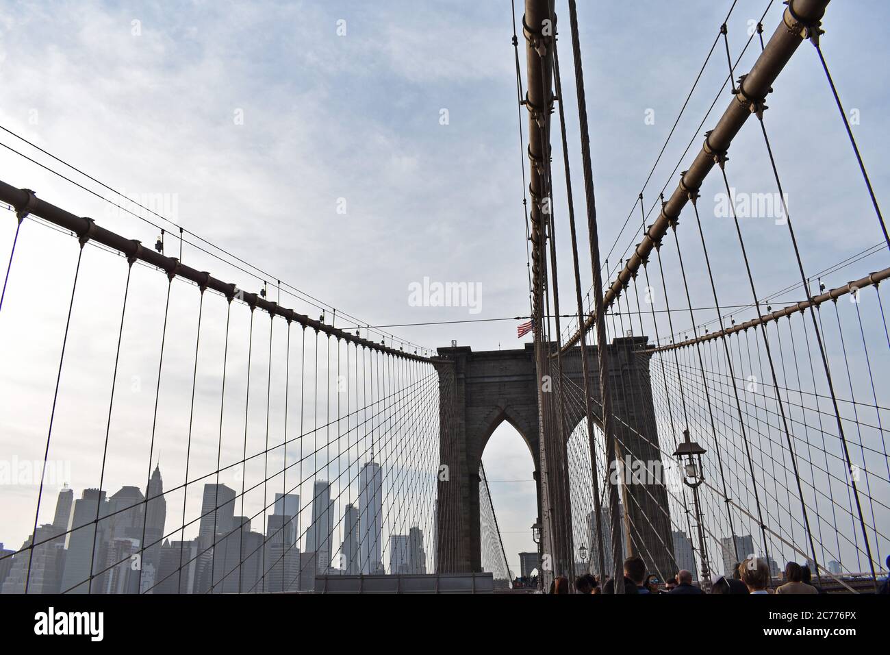 Les câbles de support du pont de Brooklyn, New York, en direction de la tour. Les gratte-ciel de New York sont visibles et les gens traversent le pont. Banque D'Images Les câbles de support du pont de Brooklyn, New York, en direction de la tour. Les gratte-ciel de New York sont visibles et les gens traversent le pont. Banque D'Images