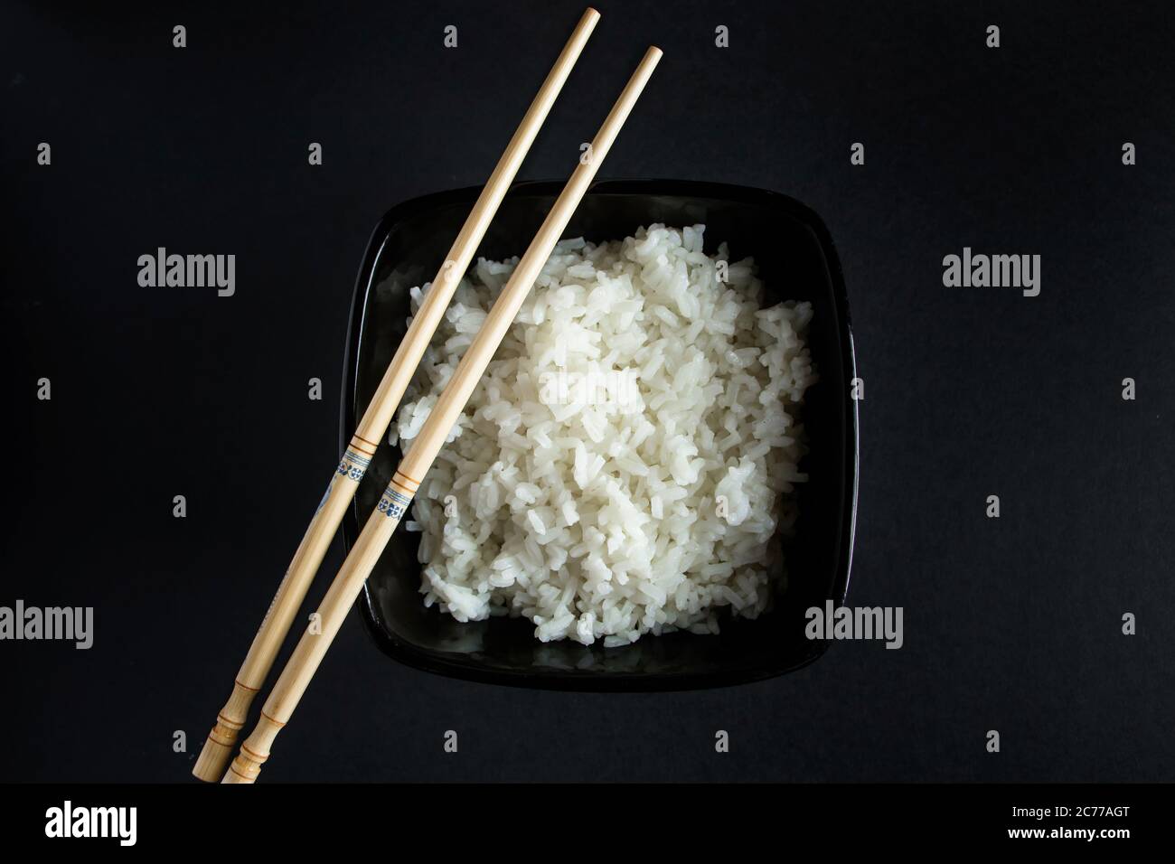 Bol avec riz bouilli sur fond noir. Cuisine asiatique et baguettes de bambou. Banque D'Images