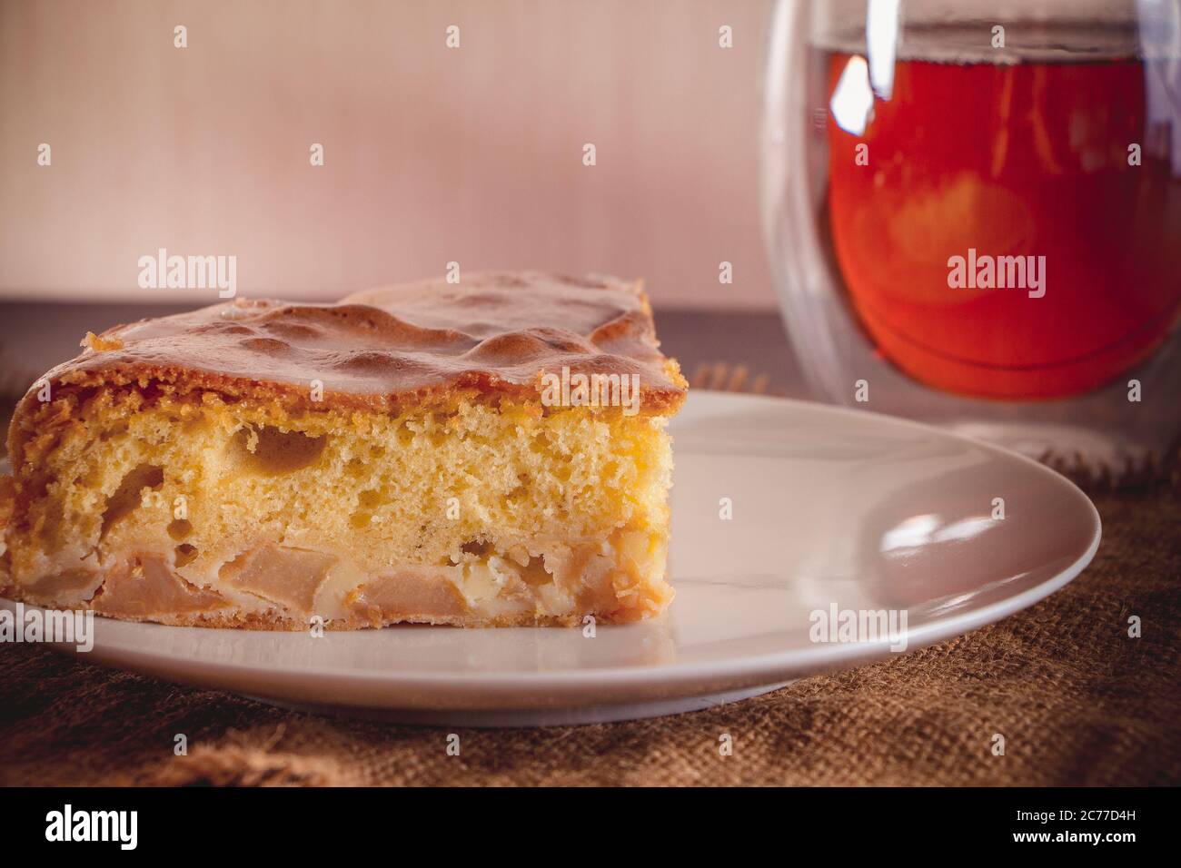 Tarte aux pommes maison sur une assiette et thé dans une tasse transparente sur fond marron chaud Banque D'Images