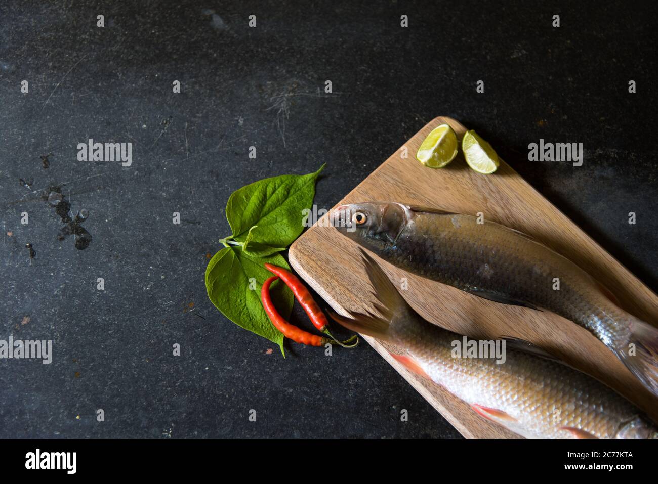 Demi-vue du poisson cru sur fond noir avec utilisation de l'accent sélectif sur une partie particulière du poisson et le reste du poisson et d'autres ingrédients bl Banque D'Images