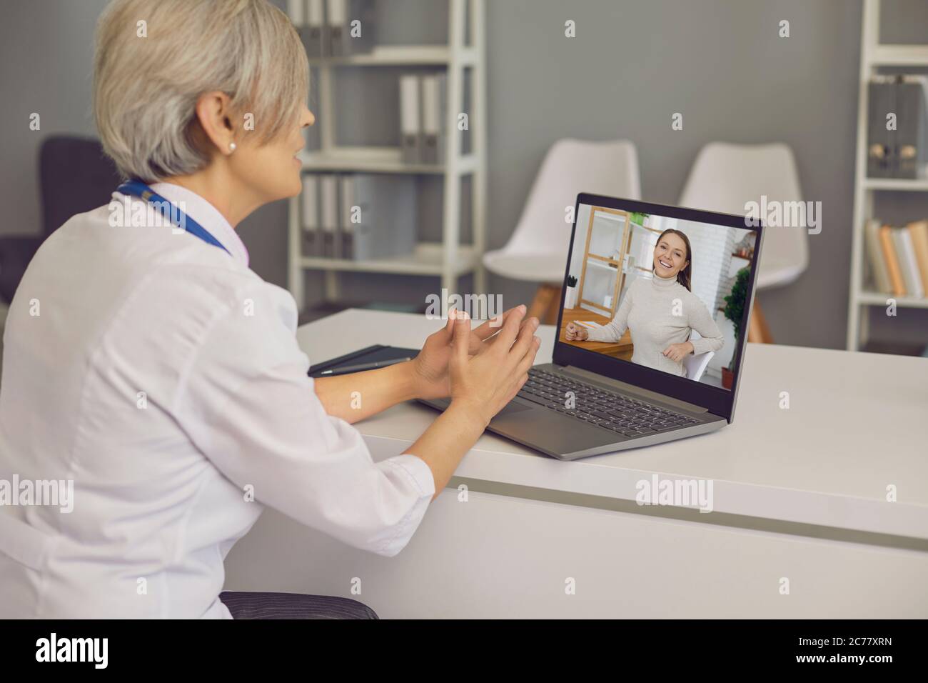 Médecin senior sur chat vidéo avec un jeune patient à l'hôpital. Medic parlant à un client sur un ordinateur portable depuis son bureau Banque D'Images