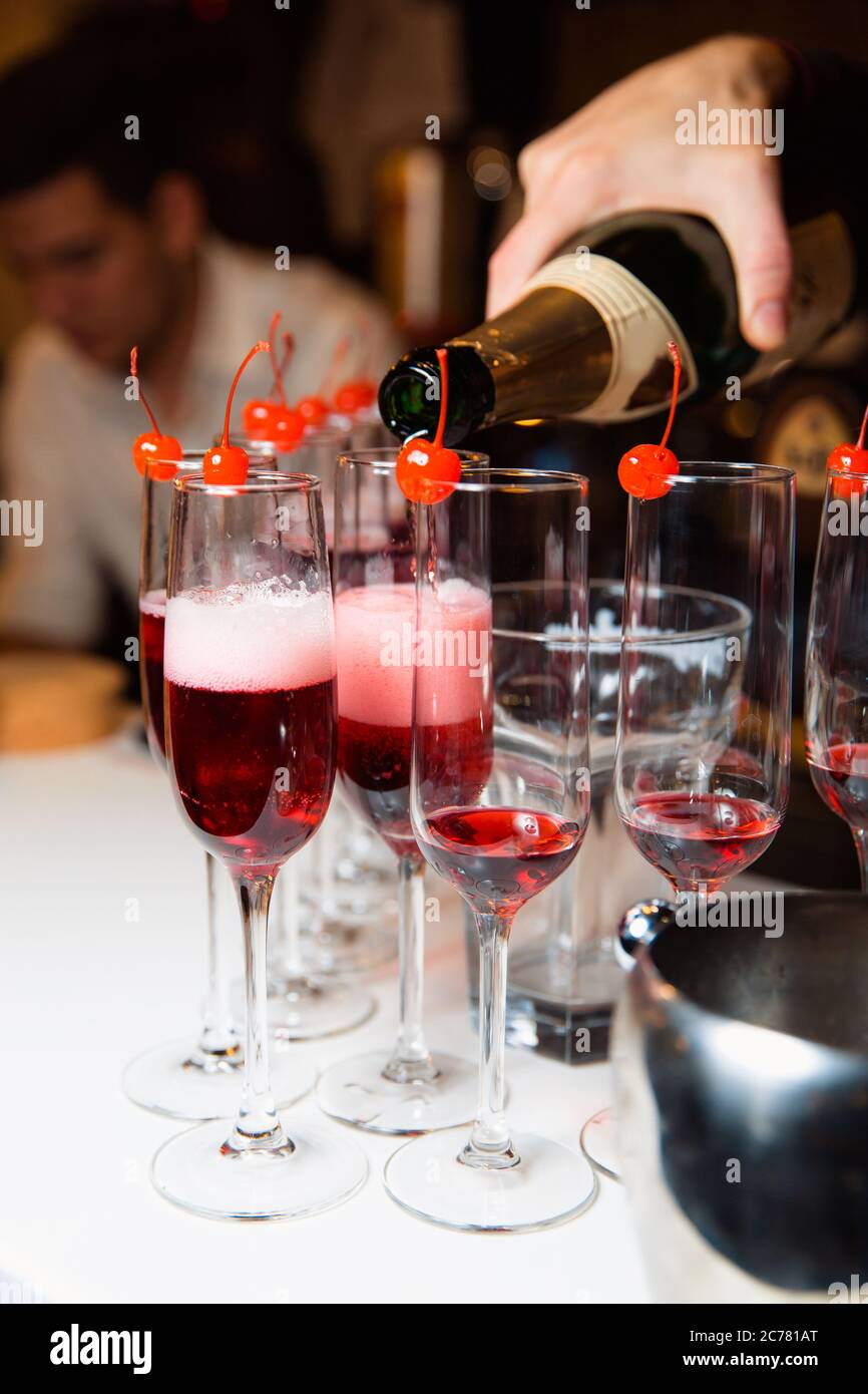 Le serveur verse du champagne dans les verres. Sur le bord du verre est une cerise. Vin mousseux à une fête. Banque D'Images