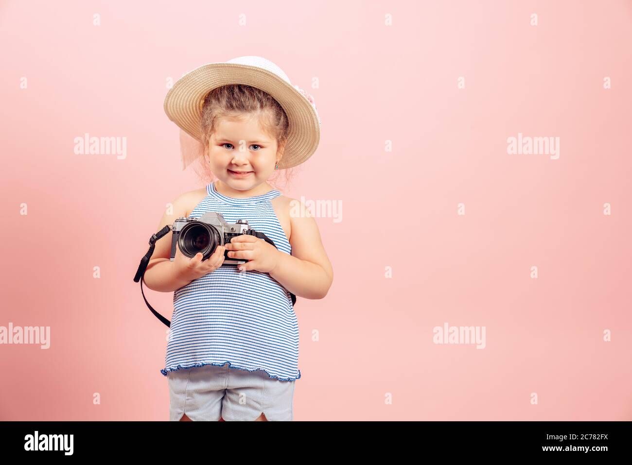 Little girl holding old vintage camera et souriant sur fond rose. Banque D'Images