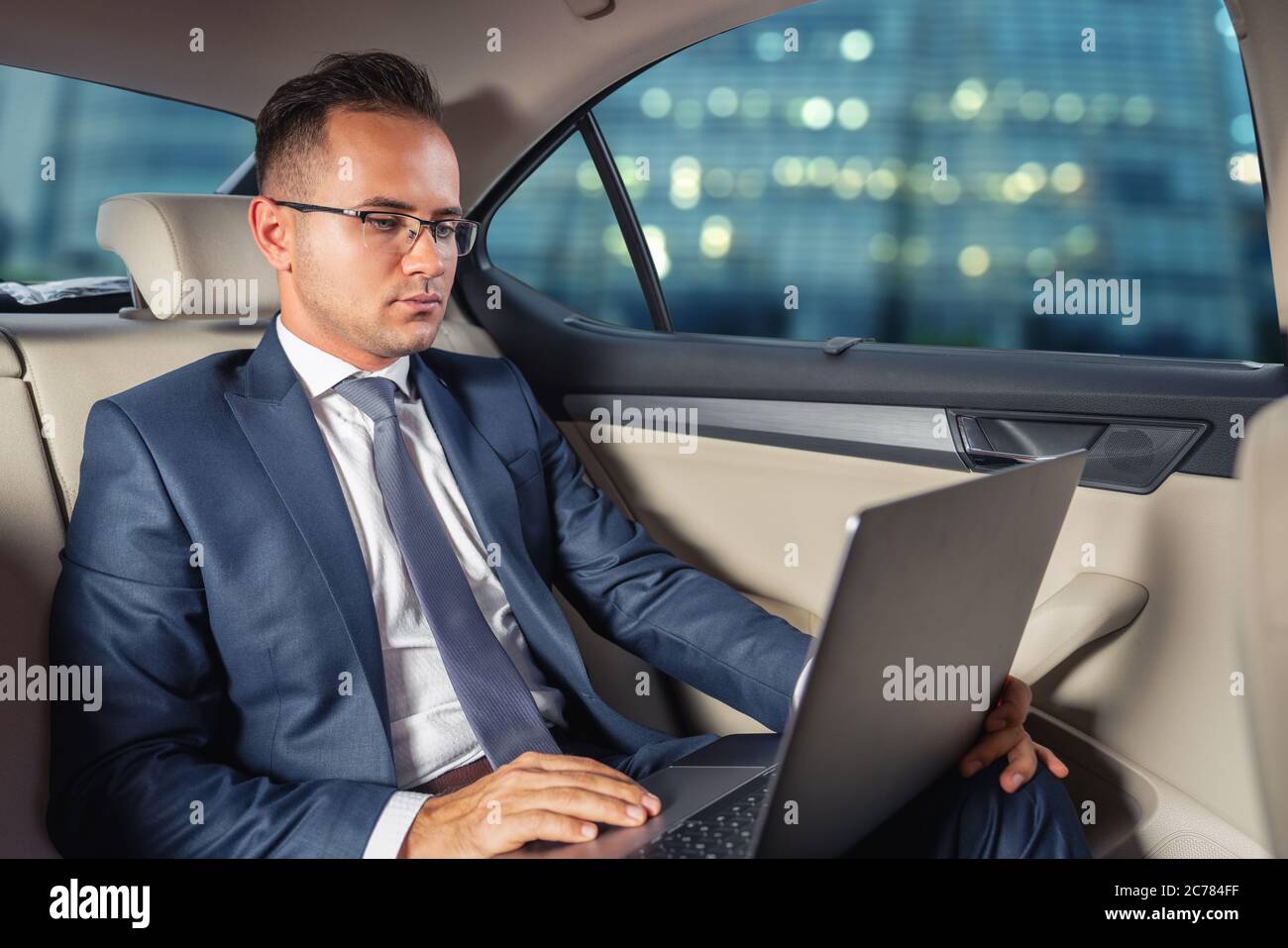 Jeune homme d'affaires utilisant un ordinateur portable dans le siège arrière de la voiture. Banque D'Images