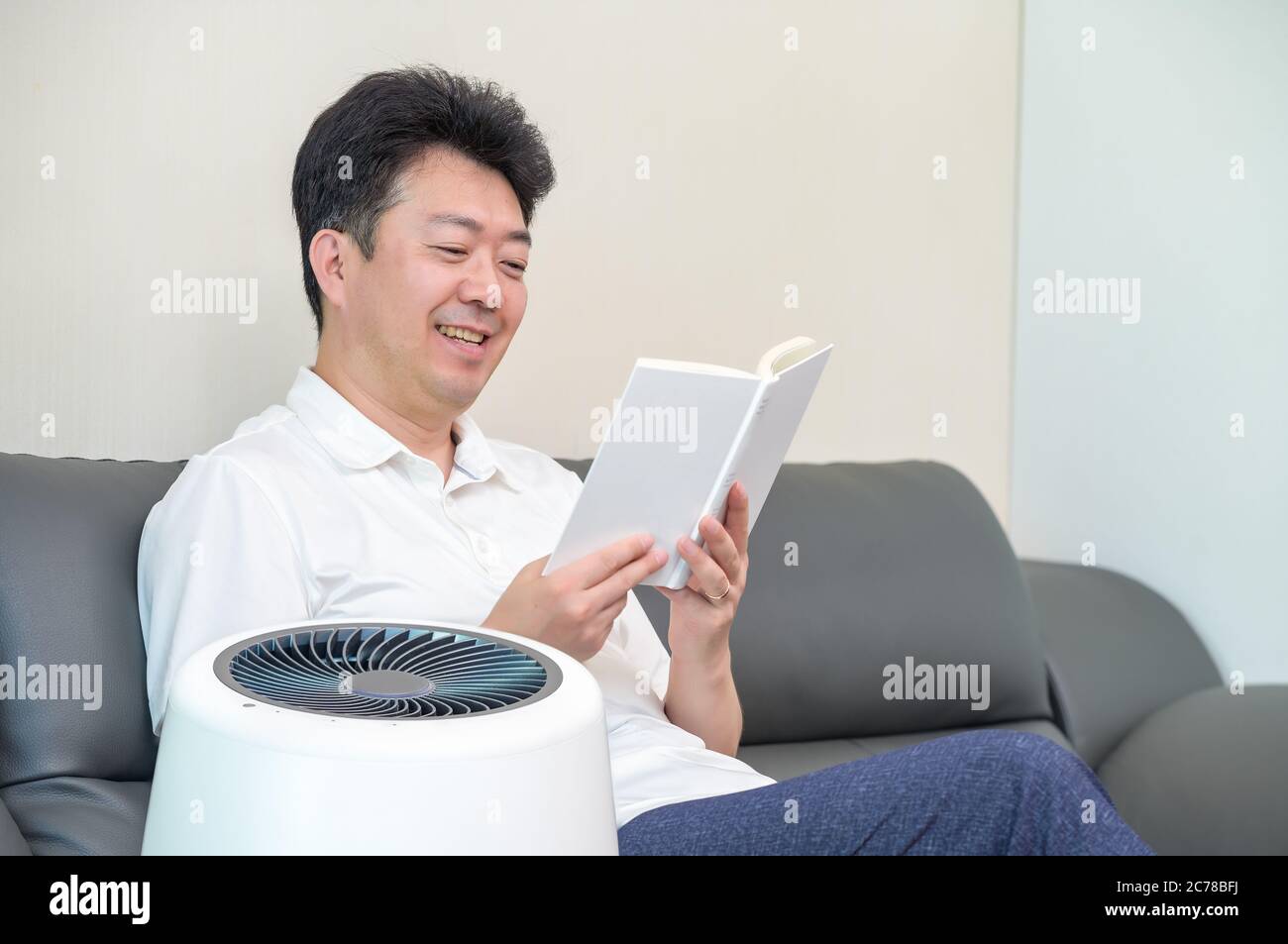 Un homme asiatique d'âge moyen lisant dans le salon avec un purificateur d'air. Banque D'Images