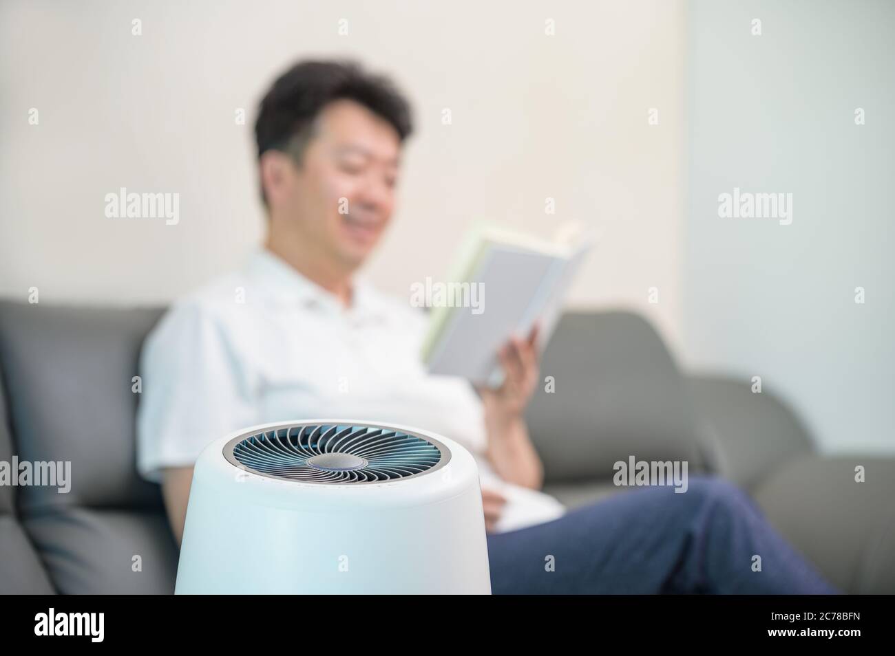 Un homme asiatique d'âge moyen lisant dans le salon avec un purificateur d'air. Arrière-plan flou. Banque D'Images