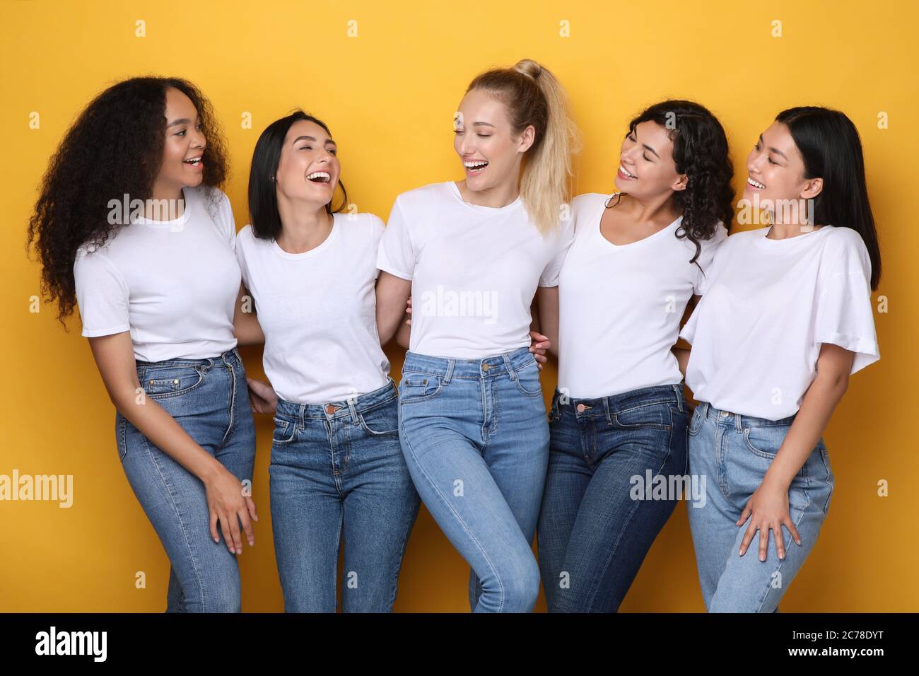 Cinq filles mixtes riant posant sur fond jaune dans le studio Banque D'Images