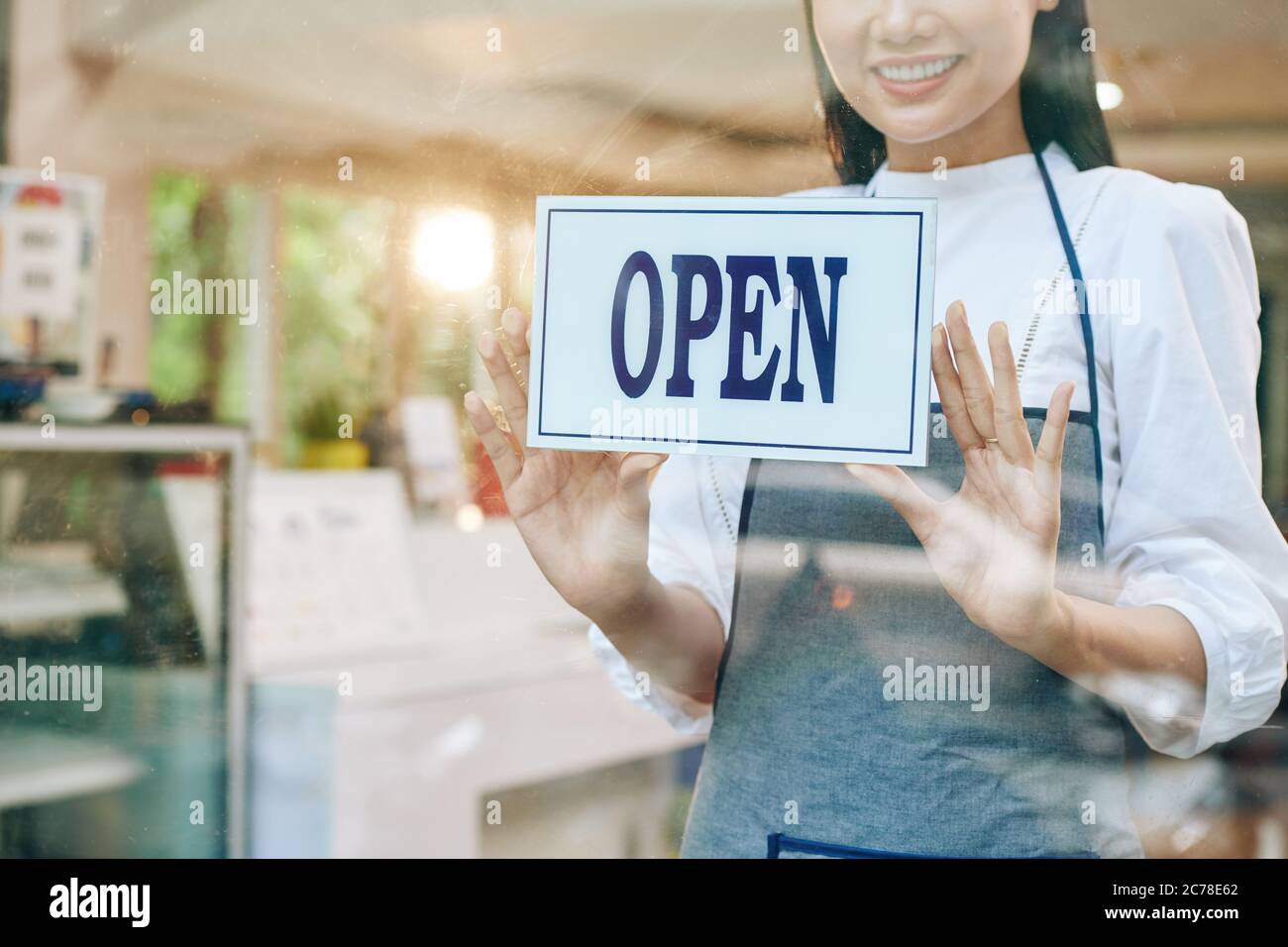 Une serveuse jeune souriante qui colle à l'affiche ouverte sur la porte en verre du coffeeshop Banque D'Images