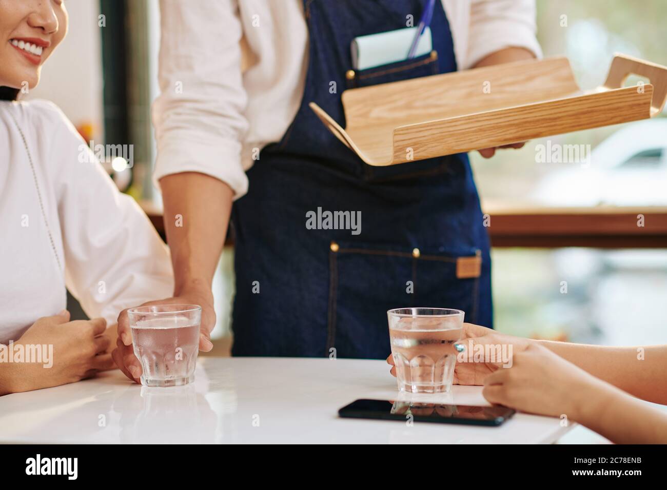 Image rognée du serveur mettant des verres d'eau douce devant les jeunes femmes à la table du café Banque D'Images