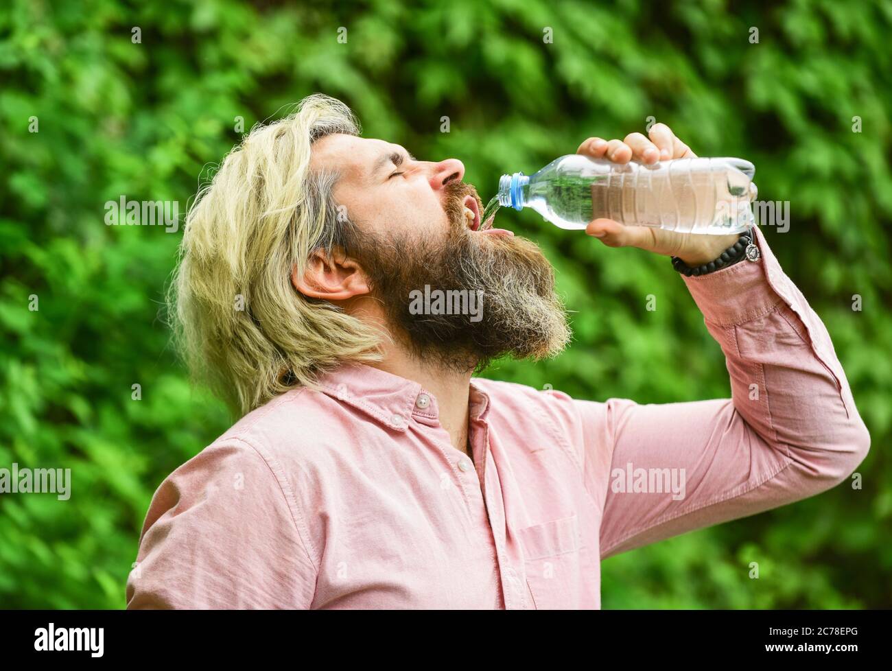 Chaleur estivale. Boire de l'eau claire. Équilibre de l'eau. Homme barbu touriste eau potable bouteille plastique nature fond. Un gars assoiffé qui boit de l'eau en bouteille Un mode de vie sain. Sécurité et santé. Banque D'Images