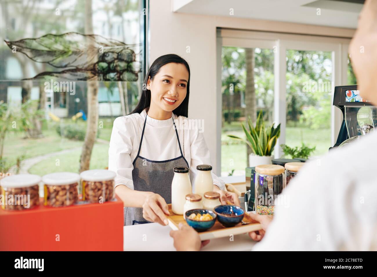 Petite serveuse de café donnant un plateau avec du yogourt non laitier, du lait et des bols de céréales au client Banque D'Images