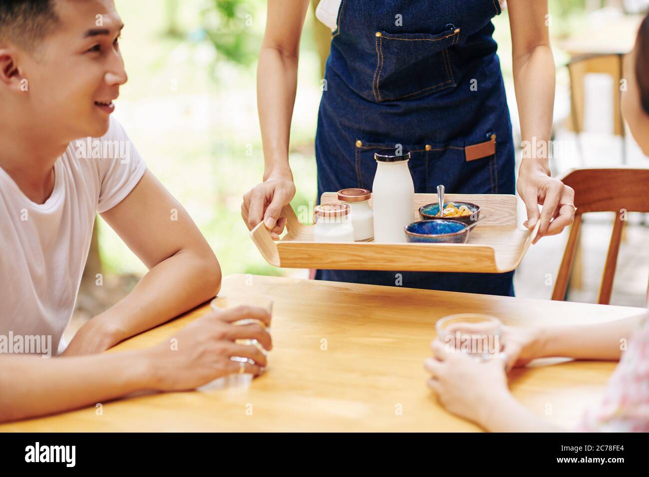 Image rognée de serveuse servant le petit déjeuner composé de yaourt frais délicieux et de céréales pour jeune couple Banque D'Images