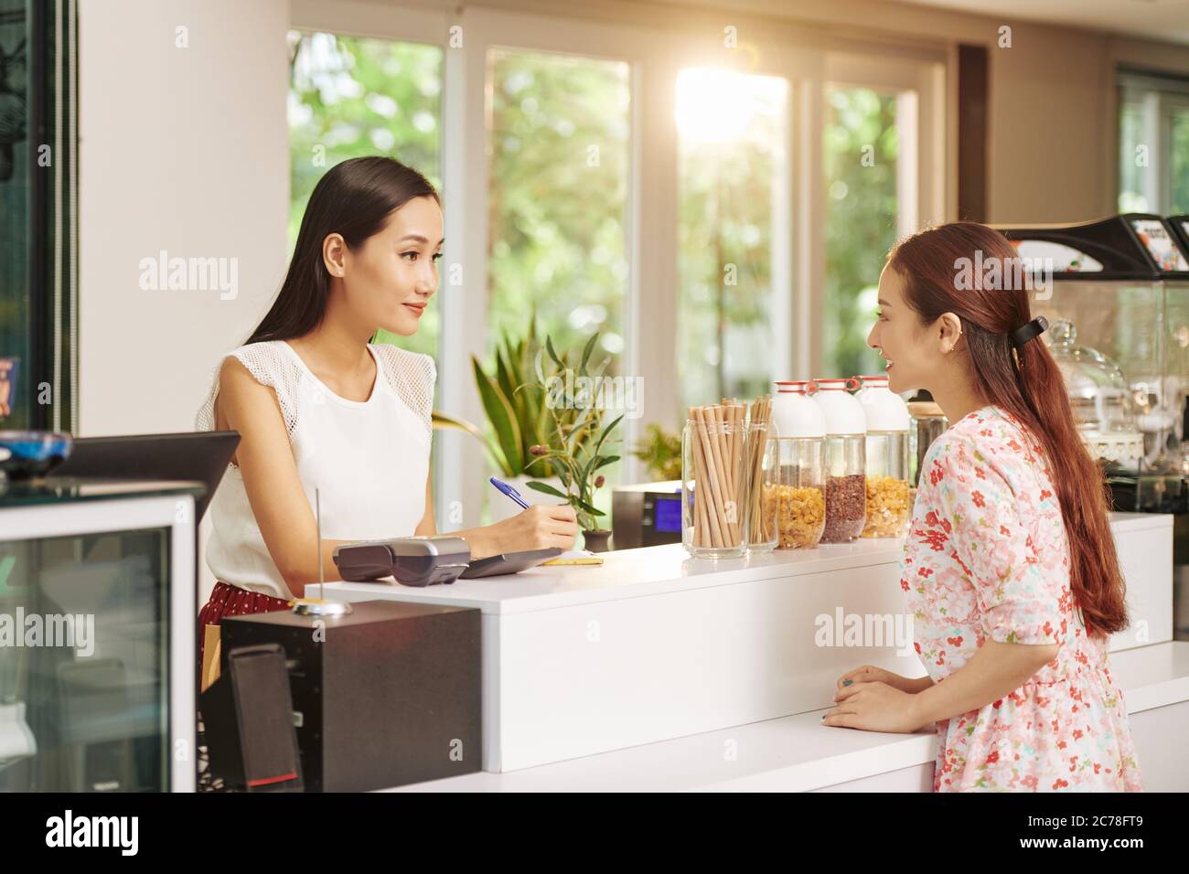 Jeune femme de barista souriante prenant des notes lorsqu'elle parle au client pour commander du café et le petit déjeuner Banque D'Images