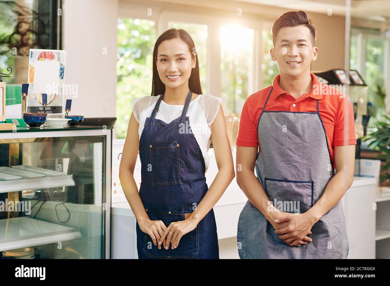 Portrait d'une équipe heureuse de serveurs en tabliers debout au comptoir prêt à rencontrer les clients après avoir ouvert à nouveau le café après la quarantaine Banque D'Images
