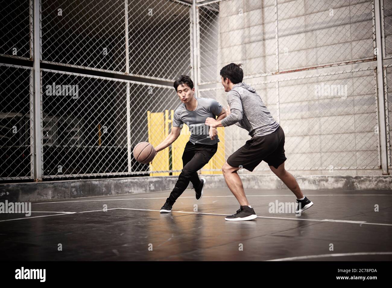 deux jeunes hommes adultes asiatiques jouant au basketball en tête-à-tête sur un terrain extérieur Banque D'Images