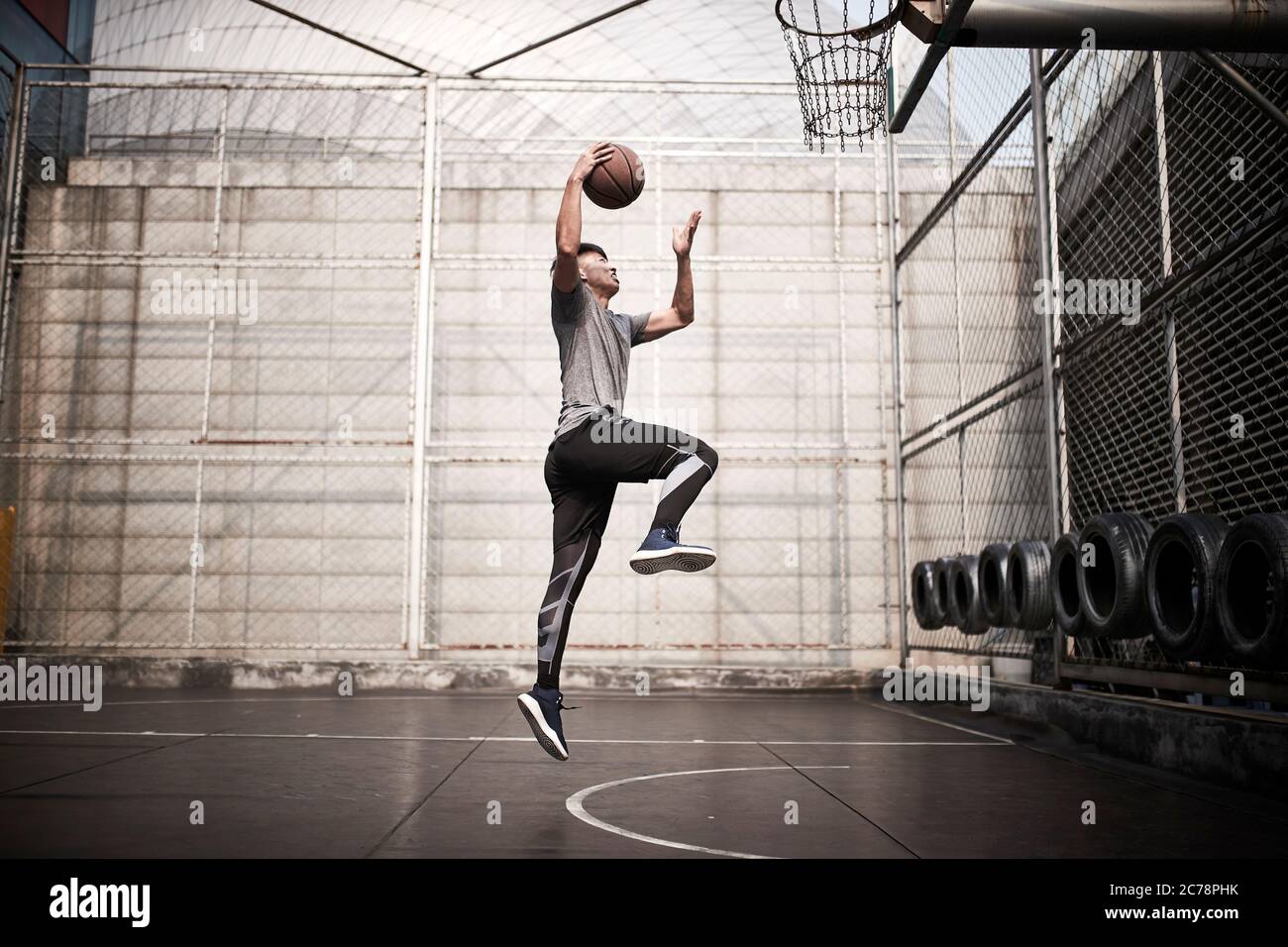 un jeune homme asiatique essaie de jouer un dunk sur un terrain extérieur Banque D'Images