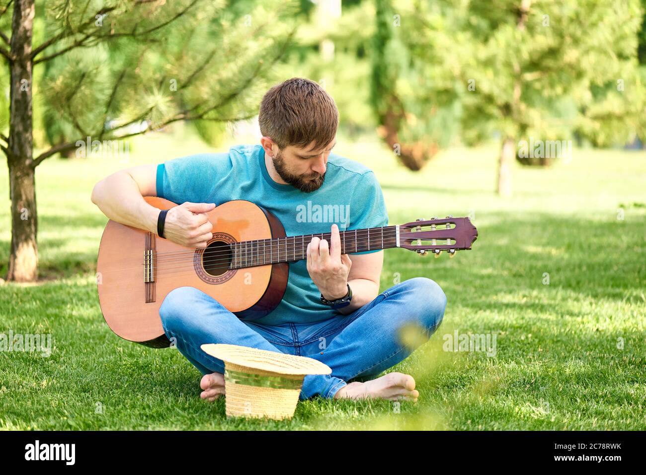 Jeune homme avec une guitare sur l'herbe verte dans le parc en été ensoleillé. Banque D'Images