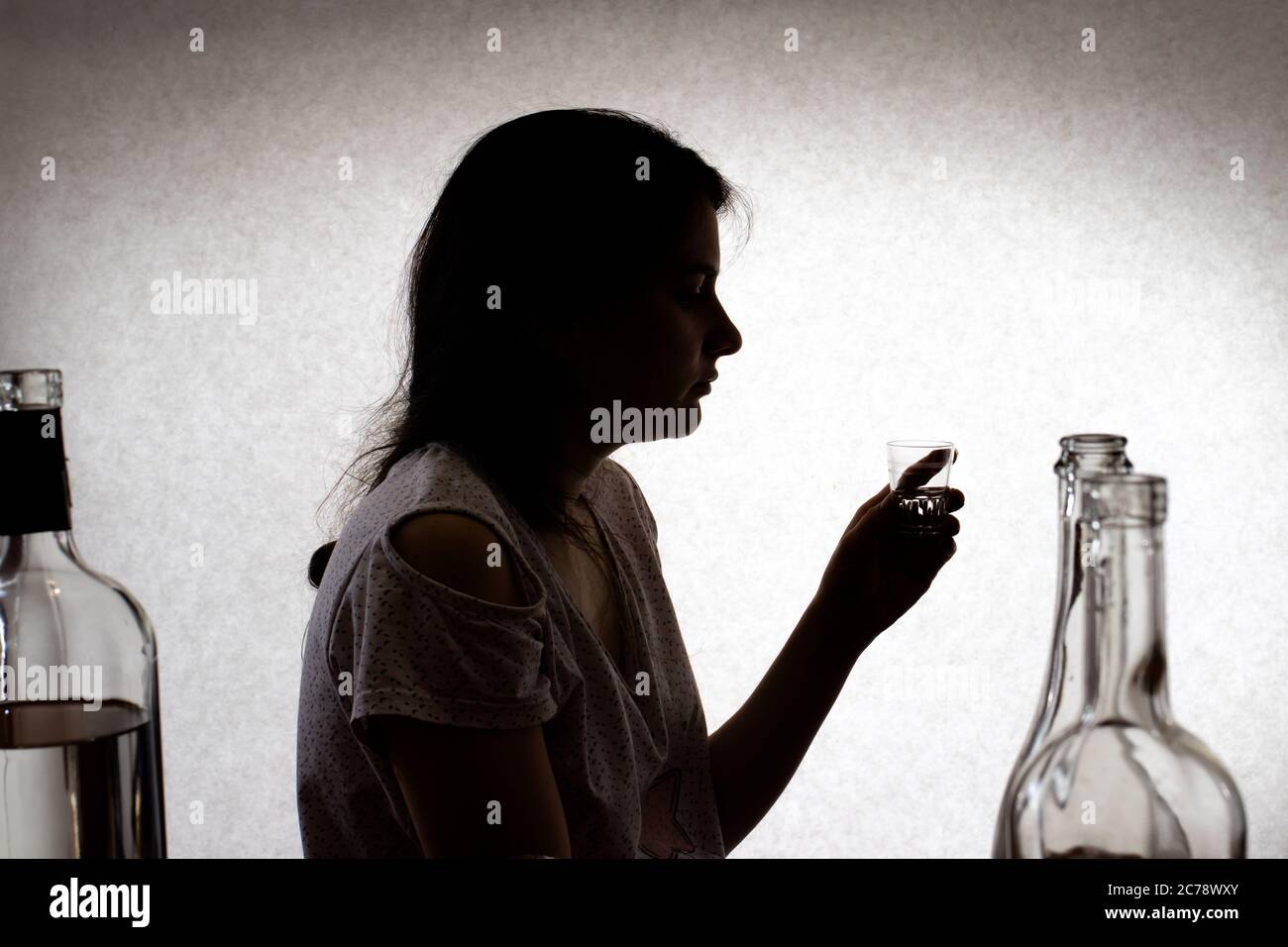 La femme tient un verre avec de l'alcool fort. Alcoolisme féminin, dépendance à l'alcool, délire tremens. Photo de silhouette. Banque D'Images