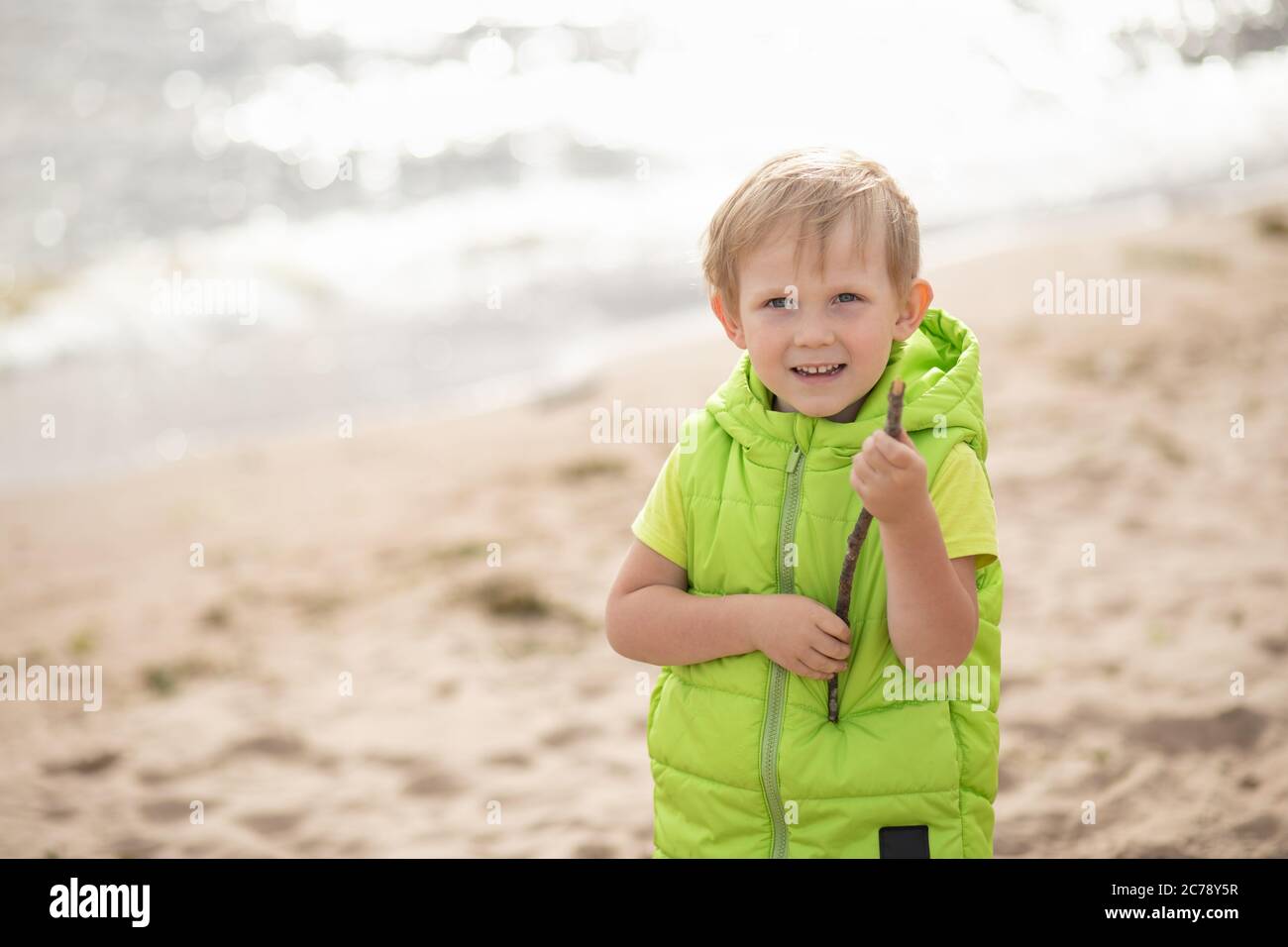 Garçon blond sur la plage sur fond de mer et de sable avec un morceau de bois dans sa main. L'idée d'une enfance heureuse et jeux, détente et travée Banque D'Images