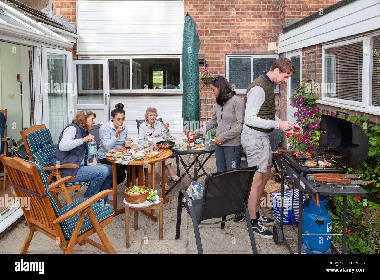Une famille de trois générations ayant un barbecue familial à la maison dans le jardin arrière, Oxfordshire Angleterre Royaume-Uni Banque D'Images