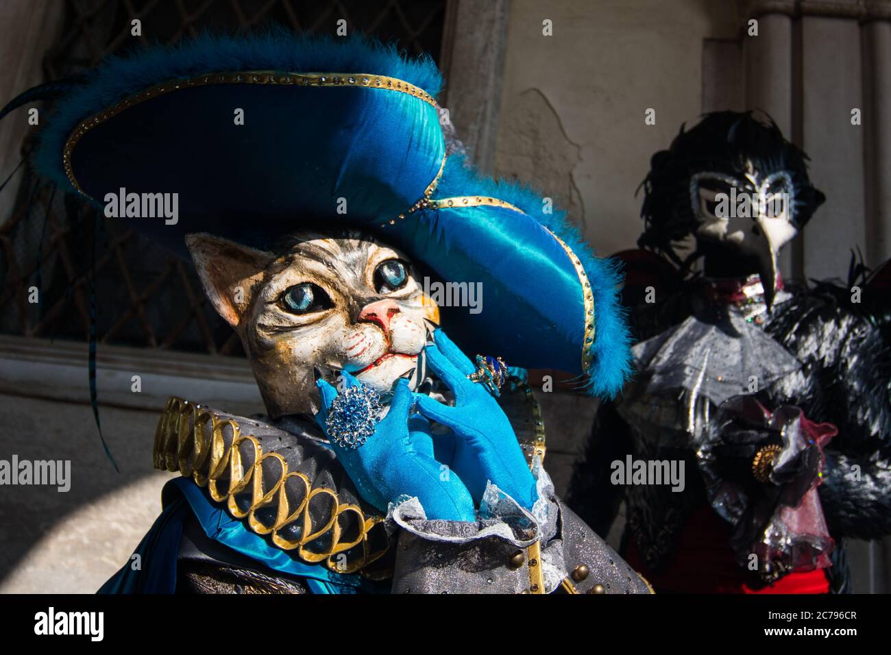 Un masque artisanal pour chat pendant le carnaval de Venise pose comme un pouss en bottes. Un autre masque noir de corbeau se pose derrière lui. Banque D'Images