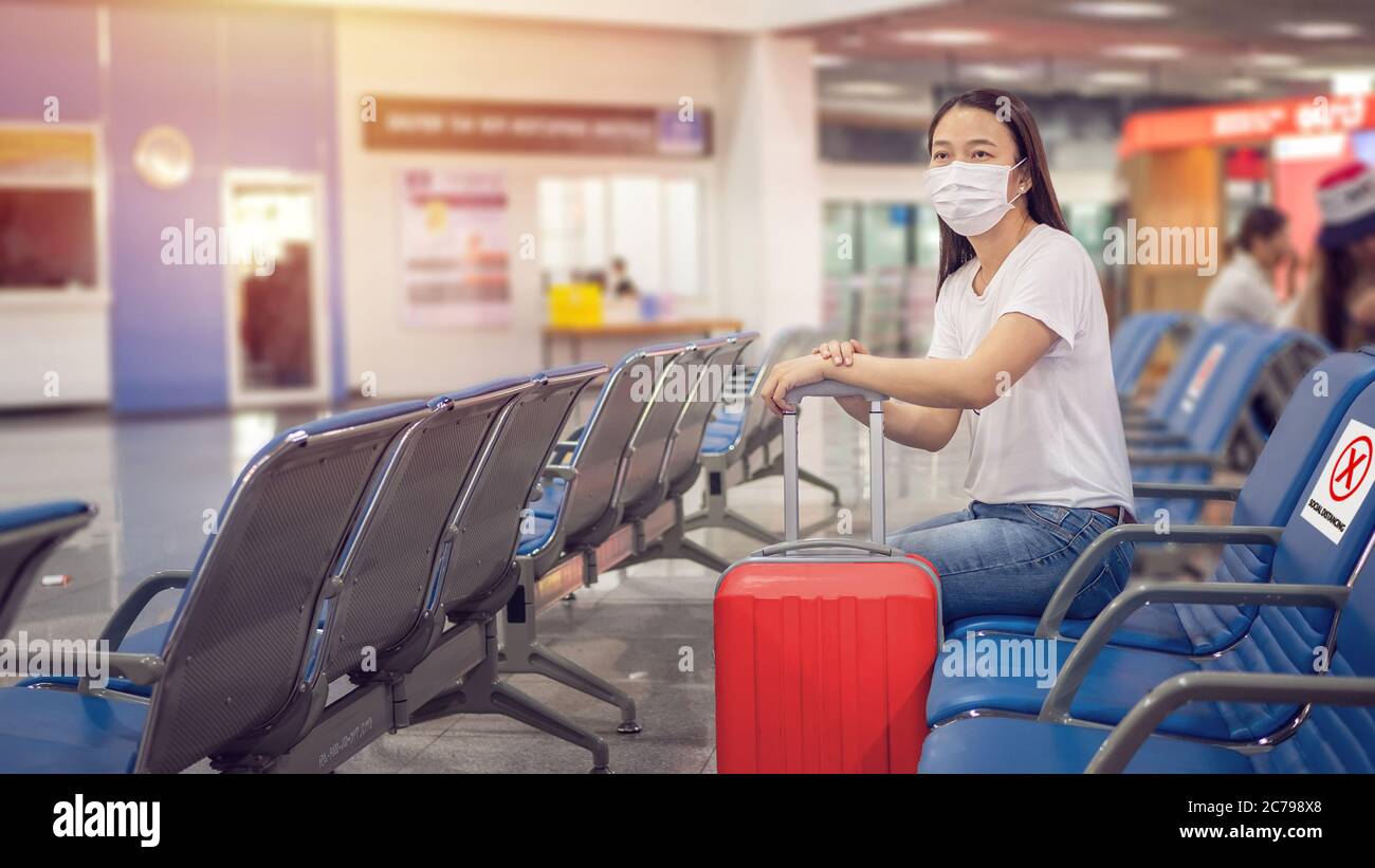 Touriste asiatique avec des bagages, portant un masque et s'asseoir sur une chaise avec une distanciation sociale pour éviter une pandémie pendant le voyage à l'aéroport. Nouvelle norme Banque D'Images
