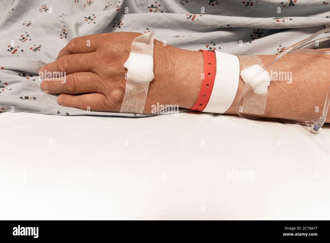 Poignet et main d'un homme dans un lit d'hôpital, bandages, bracelets, lignes IV, feuille blanche espace de copie médical antécédents médicaux, aspect horizontal Banque D'Images