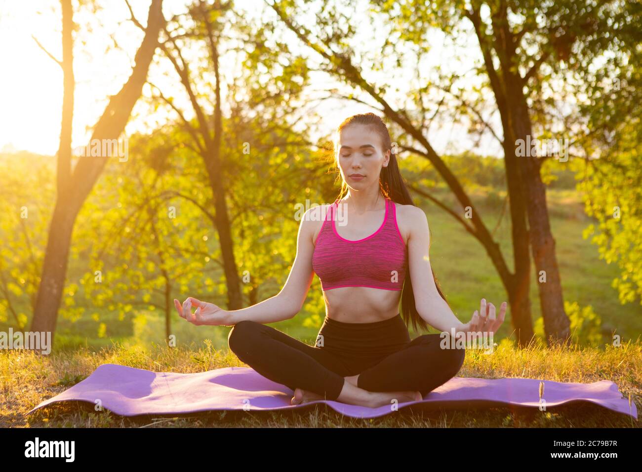 La fille est assise avec les yeux fermés sur un tapis doux. Banque D'Images
