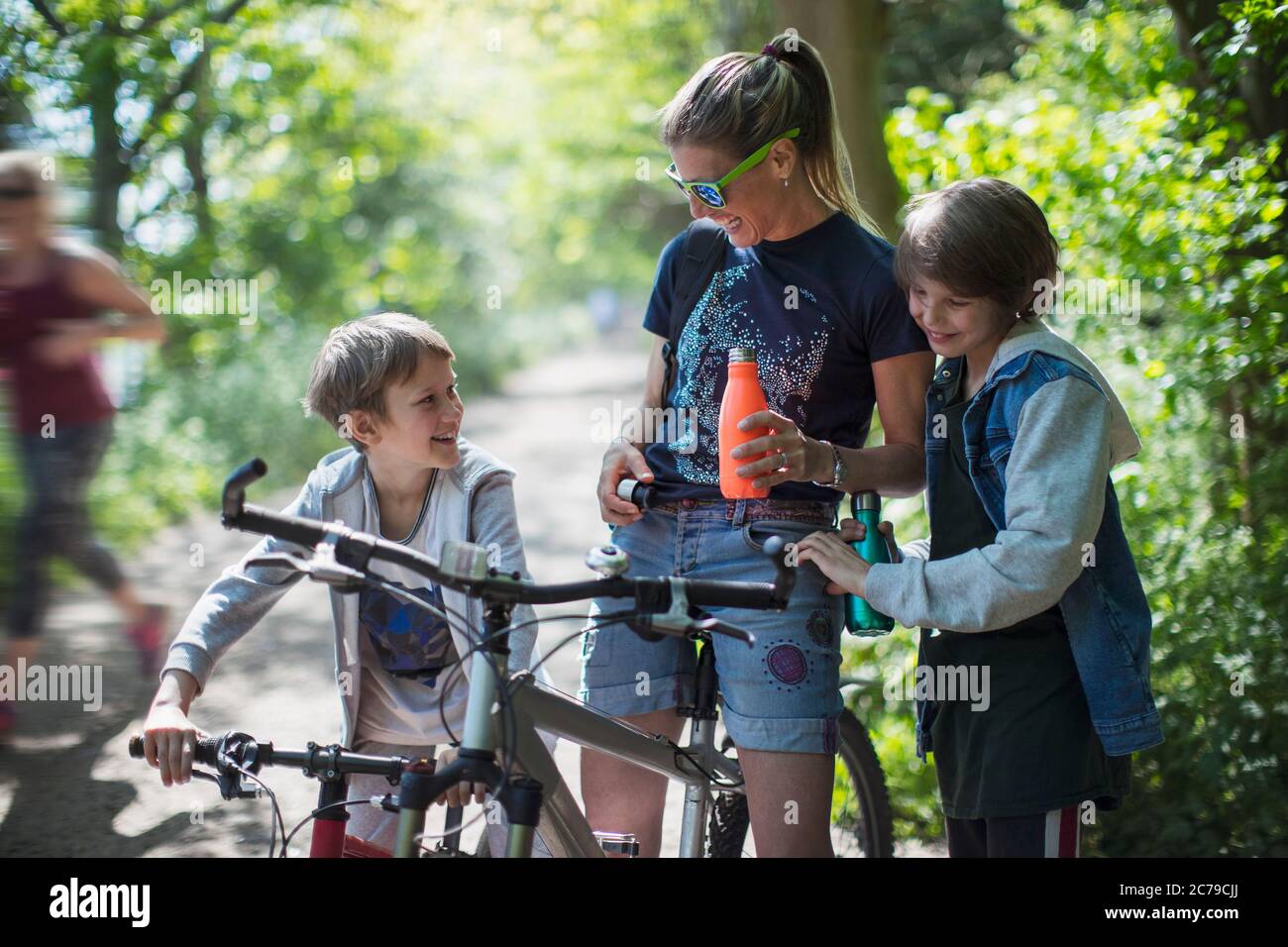 Mère et fils buvant de l'eau sur une promenade en vélo dans un parc ensoleillé Banque D'Images