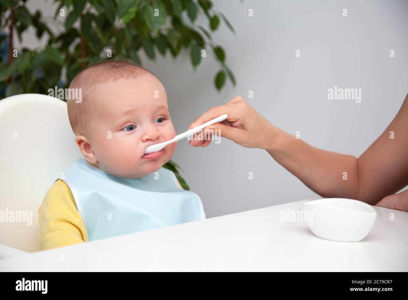 Premier Repas De Bebe Garcon Mignon A Yeux Bleus Dans Des Vetements De Couleur Jaune Bavoir Bleu Mangeant Du Yaourt Cuillere De Conservation Pour Maman Bouche Sale Sur Fond Blanc O Photo