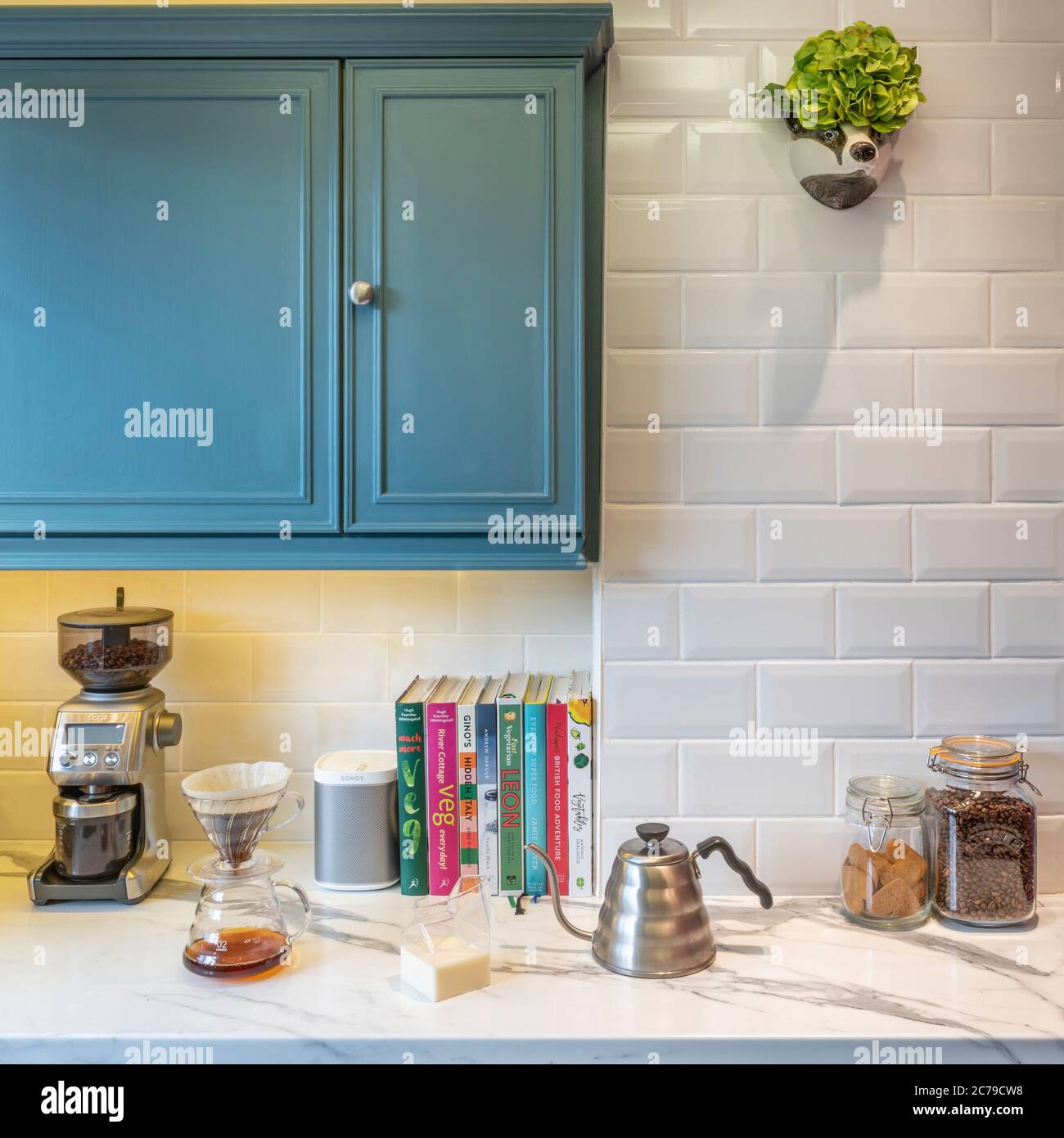 Cuisine avec mur en carrelage blanc et plan de travail en marbre. Moulin à café et bouilloire à égoutter hario sur le côté avec haut-parleur sonos Banque D'Images