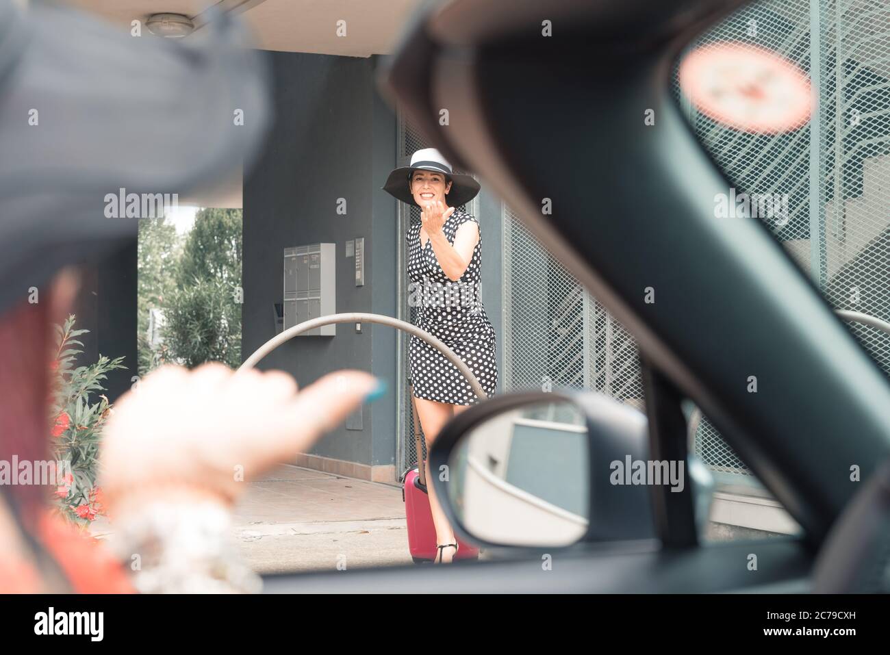 Femme élégante en robe miniature avec de hautes encoches marchant vers la voiture avec la valise. Banque D'Images