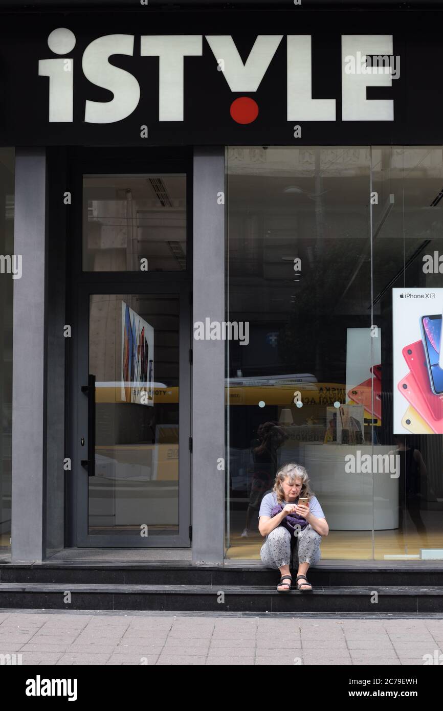 Une femme assise devant un magasin mobile tenant son nouveau téléphone. Banque D'Images