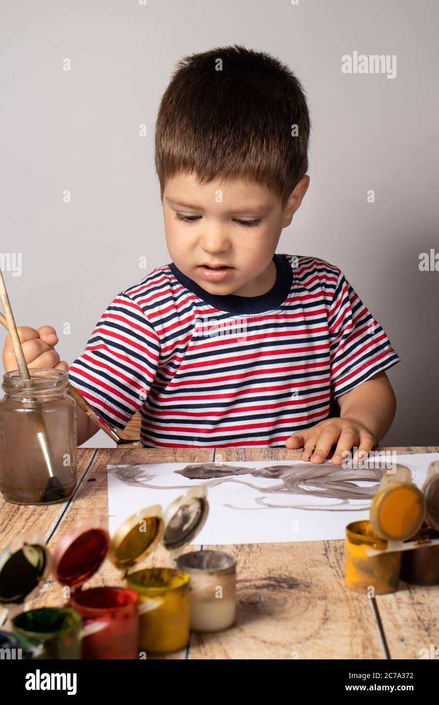 Un petit garçon de 2-3 ans dans un t-shirt rayé brillant peint une image des couleurs de la gouache. Dessin coloré, créativité des enfants. Banque D'Images