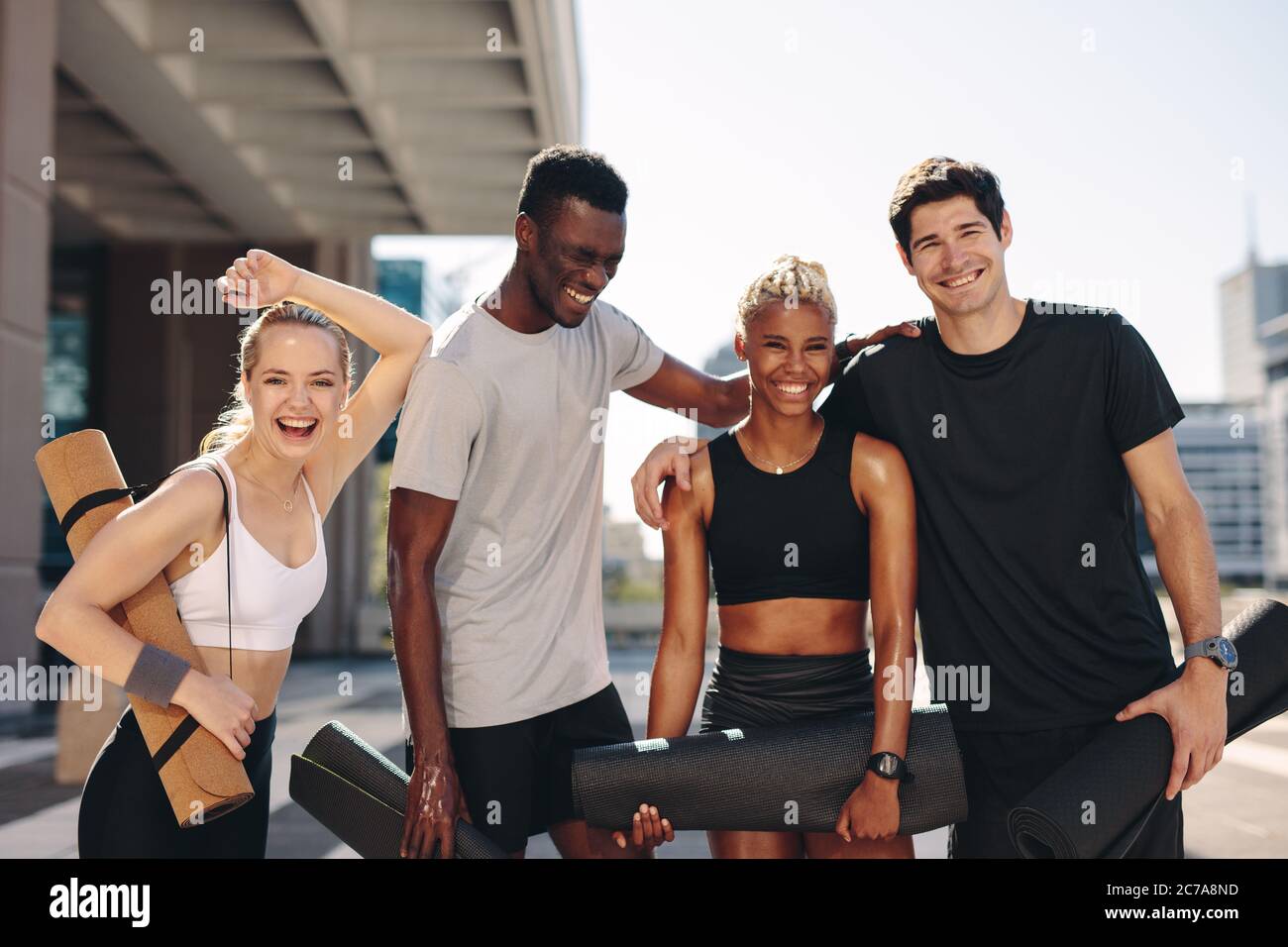 Amis multiethniques avec tapis de fitness debout à l'extérieur après l'entraînement. Groupe de fitness souriant après l'entraînement. Banque D'Images