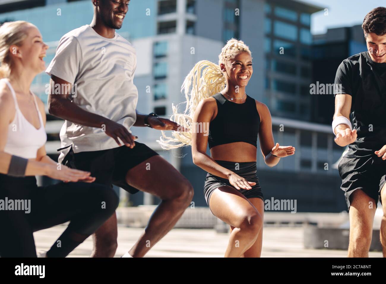 Groupe d'hommes et de femmes qui font de l'exercice ensemble dans la ville. Des amis multiethniques s'entraîner ensemble et souriant. Courir au même endroit. Banque D'Images