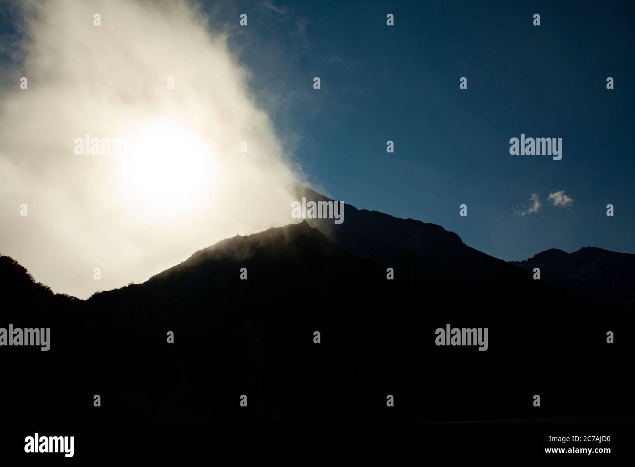 Le brouillard roule sur les eaux du lac Iliamna, en Alaska, avec le soleil projetant la lumière sur la silhouette accidentée de la montagne et le paysage sauvage serein Banque D'Images