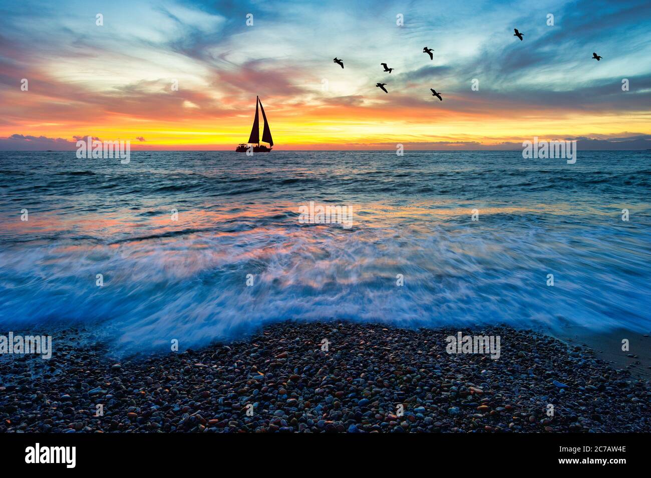 Un Voilier est la voile le long de l'océan comme un coucher de soleil coloré vif est dans l'arrière-plan Banque D'Images