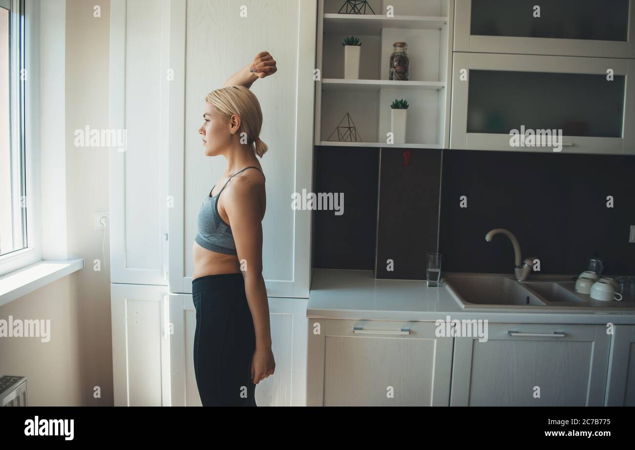 La femme blonde caucasienne portant des vêtements de sport s'étire avant de faire du yoga à la maison Banque D'Images