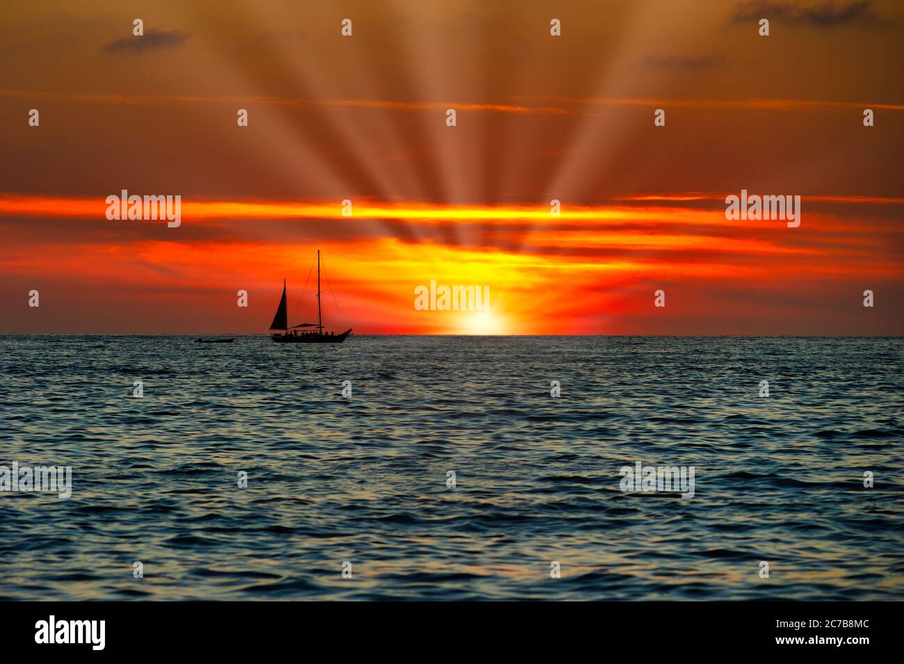Un Voilier est la voile le long de l'océan comme un coucher de soleil coloré vif est dans l'arrière-plan Banque D'Images