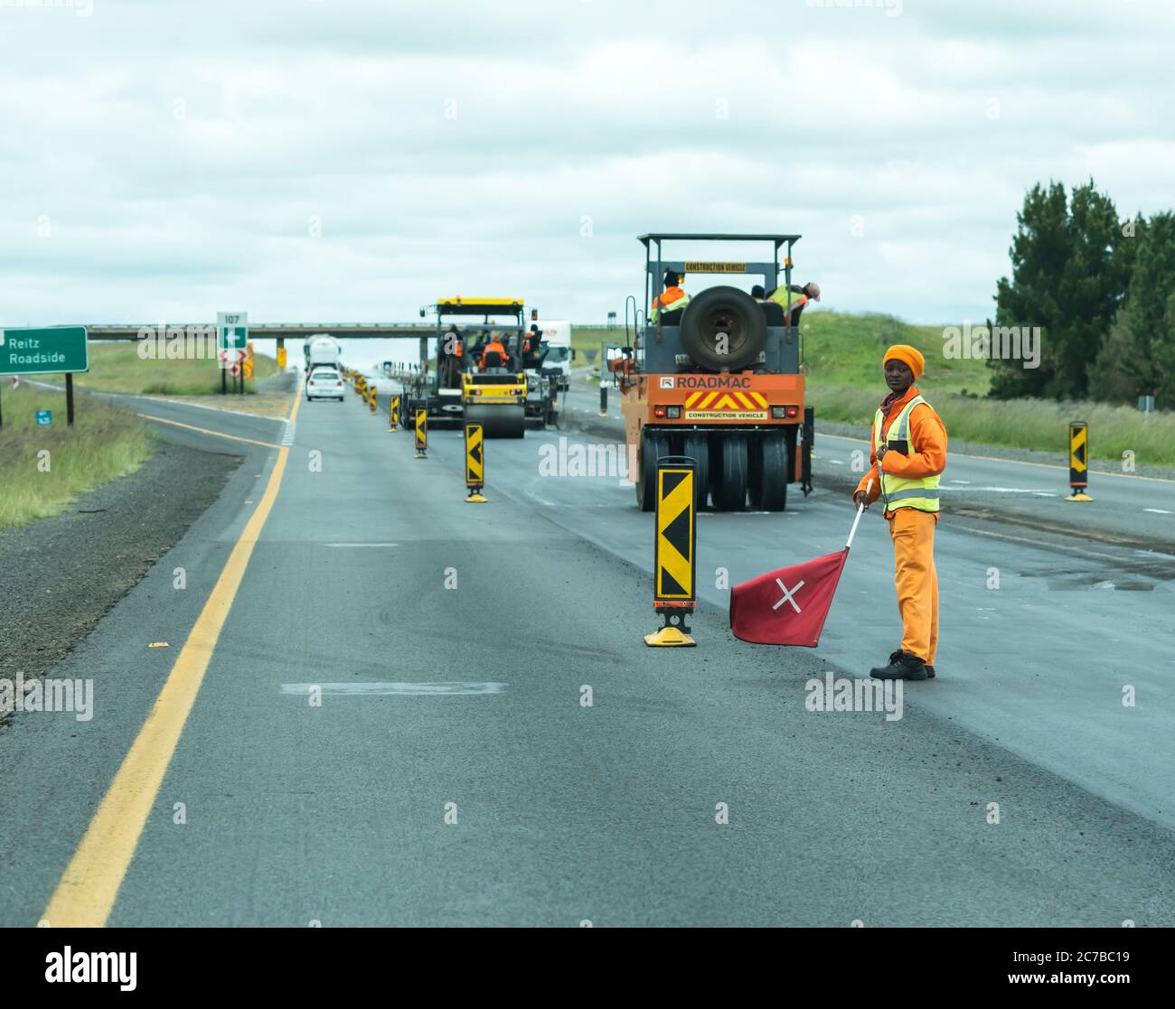 Travaux routiers sur une route sud-africaine ou avec des équipements lourds ou des machines et un travailleur africain portant un drapeau pour la sécurité routière Banque D'Images