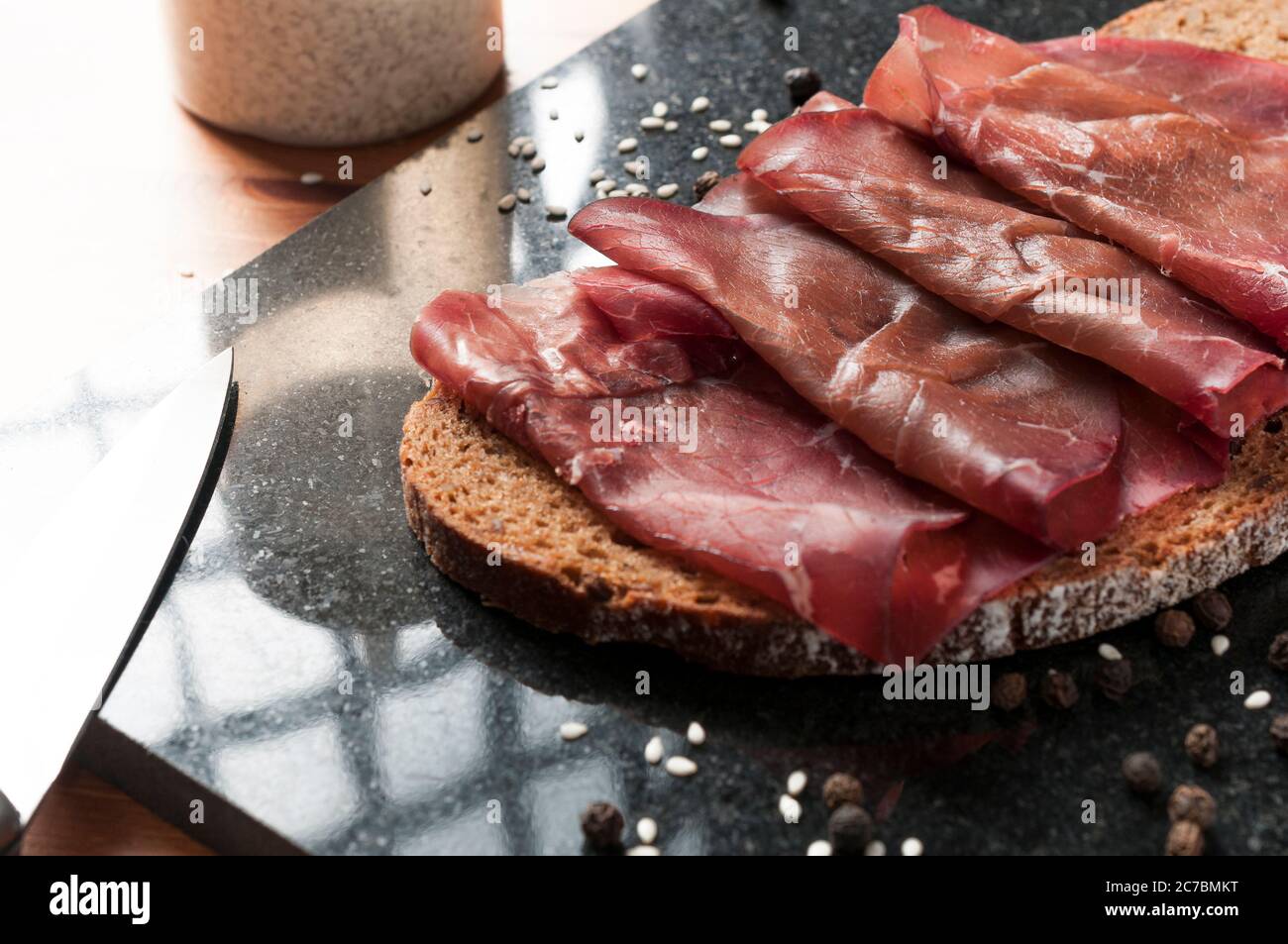 Tranche de pain complet avec bresaola (bœuf séché) sur une planche à découper en granit noir. Bresaola est un salami italien célèbre avec une teneur réduite en matières grasses Banque D'Images